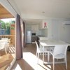 Interno di una casa mobile con tavolo, sedie, cucina e terrazza esterna in legno.