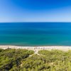 Vista aerea di una spiaggia con vegetazione costiera, mare blu e cielo sereno.