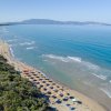 Spiaggia con ombrelloni e mare poco mosso. Vista dall'alto della costa e vegetazione.