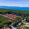 Villaggio con bungalow tra pini, mare turchese e montagne lontane.
