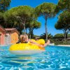 Una bambina su un gonfiabile giallo in una piscina, circondata da pini.
