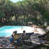Persone su sedie a sdraio e bambini in una piscina circondata da alberi.