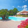 Piscina blu limpida con lettini e palme, un caffè rosa sullo sfondo in una giornata soleggiata.