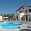 Piscina azzurra con sdraio vicino a edifici bianchi e tetti rossi sotto un cielo sereno.