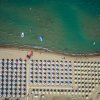 Spiaggia affollata con file di ombrelloni colorati e persone in acqua.