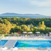 Vista di una piscina con ombrelloni bianchi, circondata da alberi e colline in lontananza.