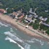 Vista aerea di una spiaggia e mare con edifici e vegetazione sullo sfondo.