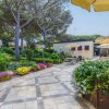 Giardino con fiori, ombrelloni gialli e sedie sotto gli alberi.