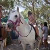 Bambini e cavalli in un'area all'aperto, con alberi sullo sfondo.