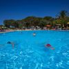 Persone che nuotano in una piscina all'aperto con ombrelloni gialli.