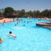Bambini giocano in una piscina all'aperto, circondata da alberi.