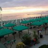 Stabilimento balneare con ombrelloni verdi e lettini sulla spiaggia al tramonto.